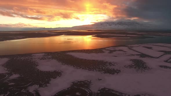 Aerial view of sunset over frozen lake panning down towards the ice alt