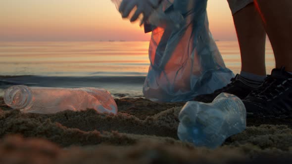 Man Collects Garbage and Plastic Bottles on the Beach alt