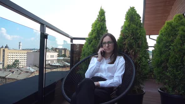 Attractive Female Freelancer Sitting on Terrace with View Over Cityscape alt