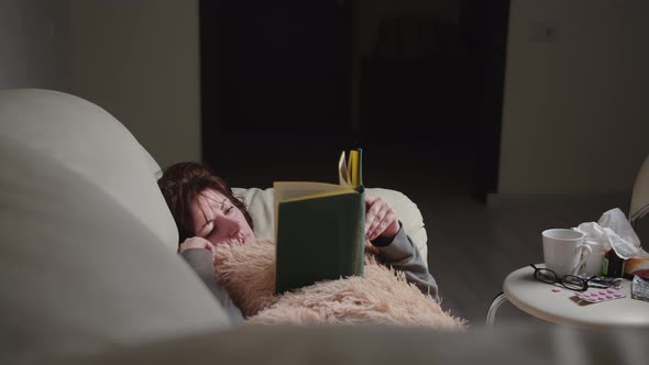Woman Is Ill at Home Lying on the Sofa Reading a Book in the Evening