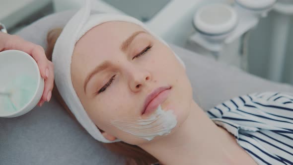 Cosmetician Hands Applying Cream Mask on Young Woman's Face at Beauty Spa Salon