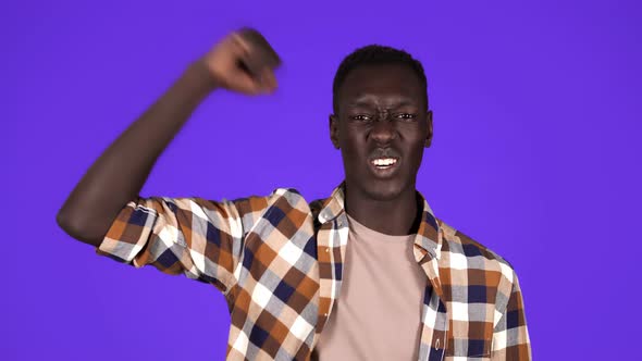 Strong Afro American Young Man Wearing Plain Shirt Isolated on Blue Background in Studio Showing alt