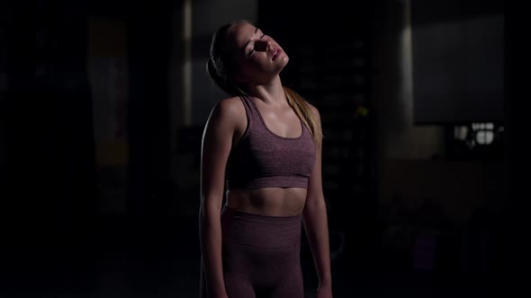 Young Sportswoman Warming Up Neck Muscles Stretching in Slow Motion Standing in Darkness alt