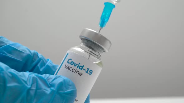 Close up of a doctor in medical blue gloves filling a syringe with a dose of coronavirus vaccine