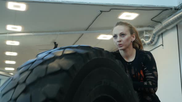 Caucasian Athlete Woman Rolls Big Tires in The Gym. Young Woman Exercising Crossfit