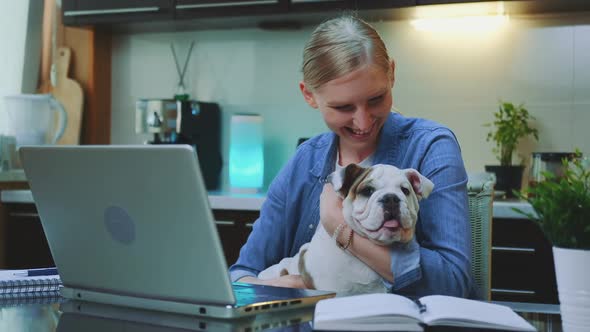Smiling Woman Stroking and Hugging the Bulldog While Sitting at the Computer alt