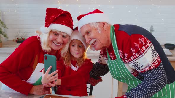 Senior Grandparents with Granddaughter Kid Taking Selfie Photo on Mobile Phone at Christmas Kitchen alt