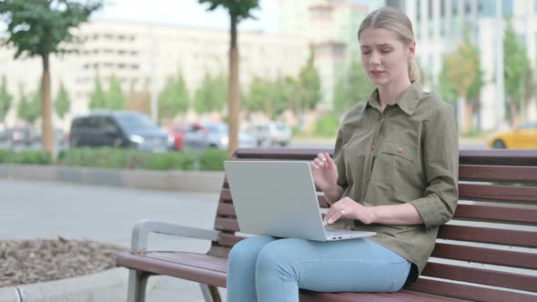 Woman with Neck Pain Using Laptop while Sitting Outdoor on Bench alt