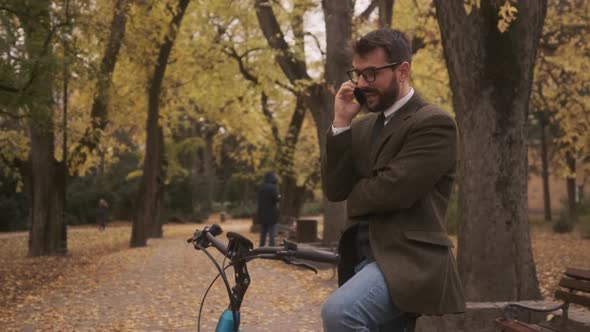 Handsome young man with electric bicycle using mobile phone in the autumn park