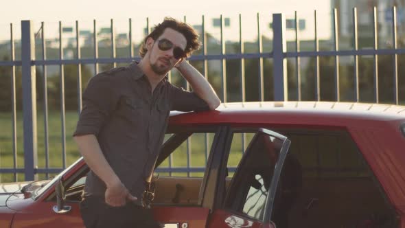 Portrait of Handsome Man with His Old Classic Powerful Car on Street at Sunset or Sunrise alt