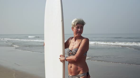 Portrait of Mature Active Pensioner Woman with Surfboard on the Sea Beach alt