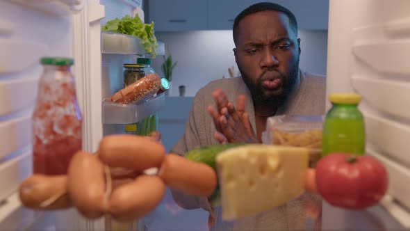 Sleepy hungry man in bathrobe at midnight opening refrigerator and taking all food, gluttony