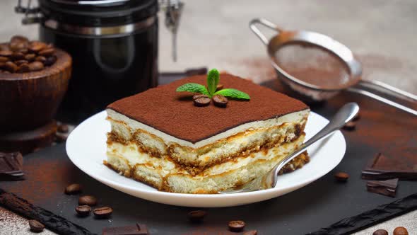 Portion of Traditional Italian Tiramisu dessert and hand coffee grinder on grey concrete background alt