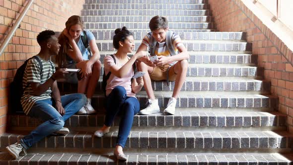 Classmates sitting on staircase and using mobile phone alt