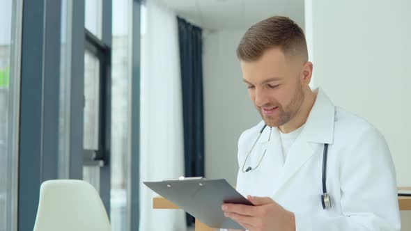 Male Doctor Writing a Patient's Medical History in His Medical Office alt