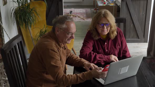 two elderly people surfing internet on laptop computer at home. alt