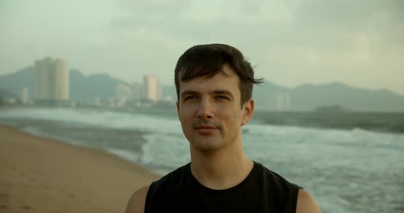 Portrait of a Young Caucasian Man Looking Into the Camera Along the Backdrop of the Beautiful Sea alt