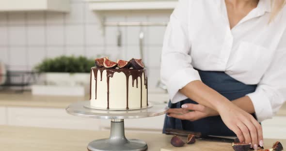 Young Beautiful Woman is Garnishing Caramel Cake or Cheesecake with Chocolate and Figs