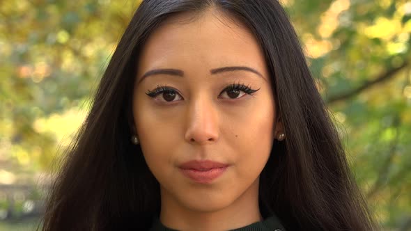 A Young Asian Woman Looks Seriously at The Camera in A Park alt