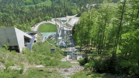 Riding a chair lift down the hill at Planica, Slovenia in the summertime with trees and ski jumps in alt