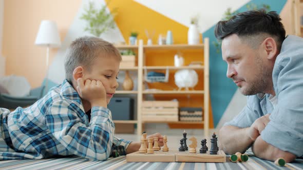 Little Kid Enjoying Chess Game with Caring Father Spending Leisure Time at Home alt