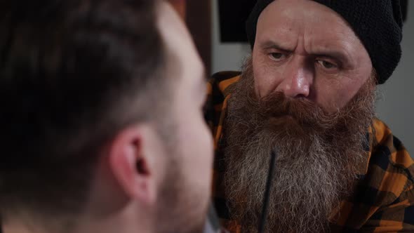 Adult Male Barber with a Long Beard Cuts the Beard of a Young Guy