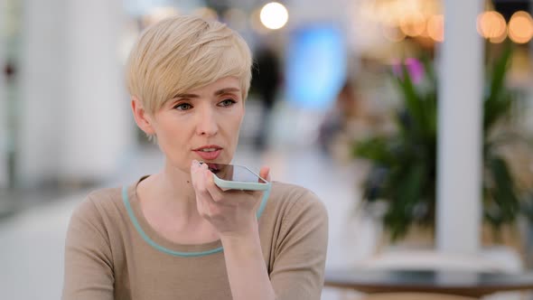 Middle Aged Adult Woman Recording Voice Recognition Message on Speakerphone in Cafe Businesswoman alt