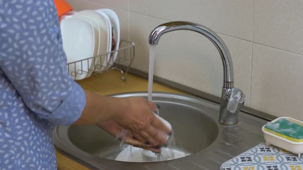Person washing dishes in the kitchen. Woman's hand washing cups. alt