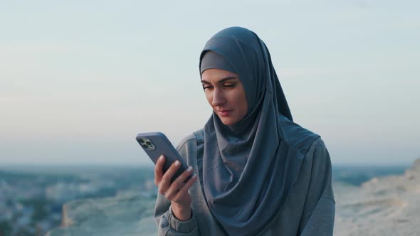 Beautiful Woman in Hijab on Top of the Hill in the Evening Uses Smartphone She Chats By Cellphone