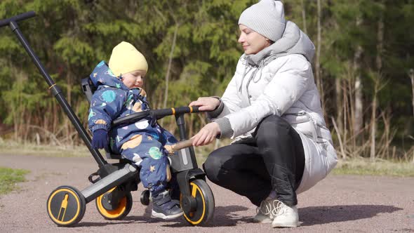 Mother with Child on a Walk in the Spring Park Kid on Toddler Tricycle Push Bike Baby Trike with alt