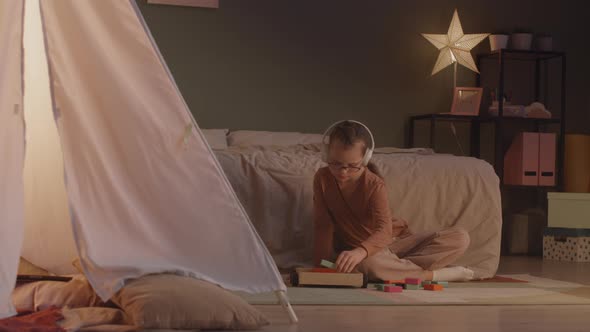Girl in Headphones Playing with Building Blocks at Home alt