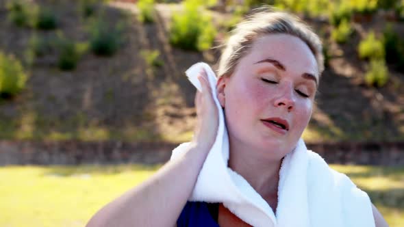 Woman wiping sweat while drinking water after workout alt