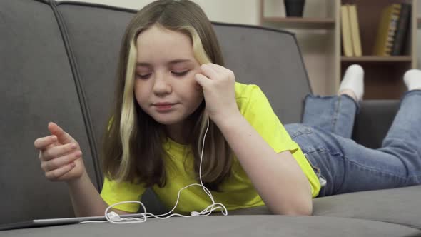 A Happy Caucasian Teenage Girl on a Comfy Couch Watching a Movie on Her Tablet alt