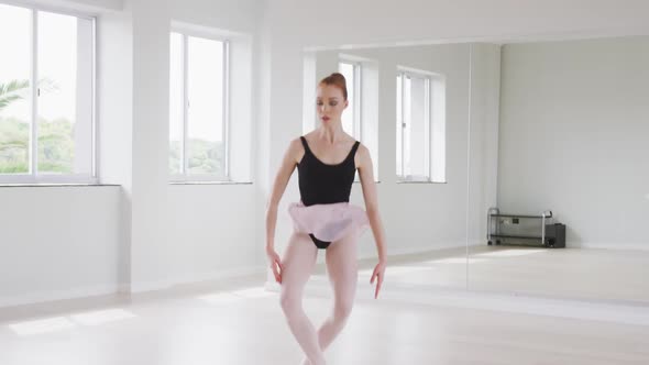 Caucasian female ballet dancer practicing ballet during a dance class in a bright studio alt
