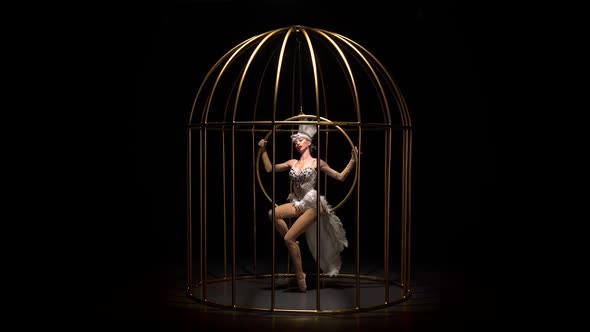 Graceful Girl in Bird Costume Riding a Hoop in a Cage on the Stage. Black Background alt