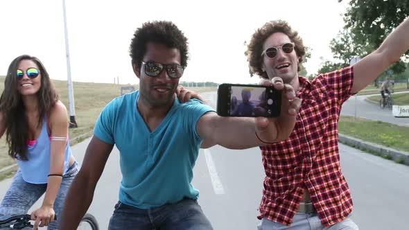 Three young adults on bikes taking selfies with phone alt