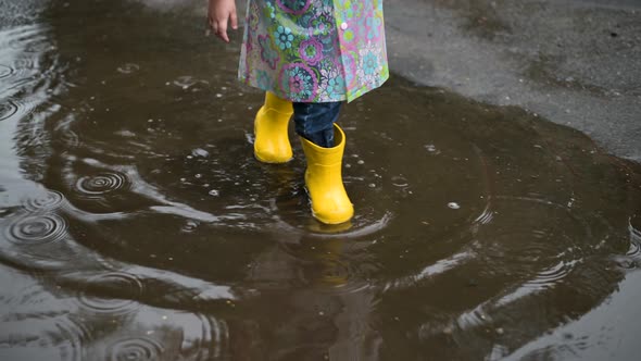 A little girl walks on the street on a rainy summer day in yellow rubber boots alt