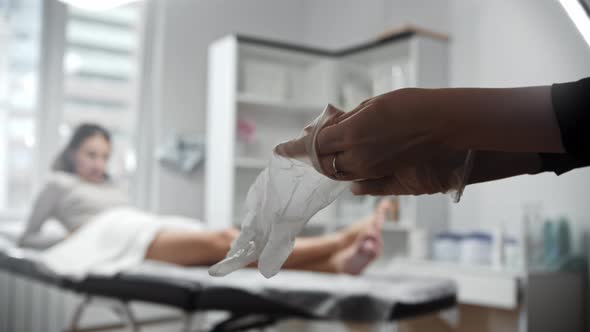 The Epilation Master Puts on Latex Gloves Before the Procedure with a Woman alt