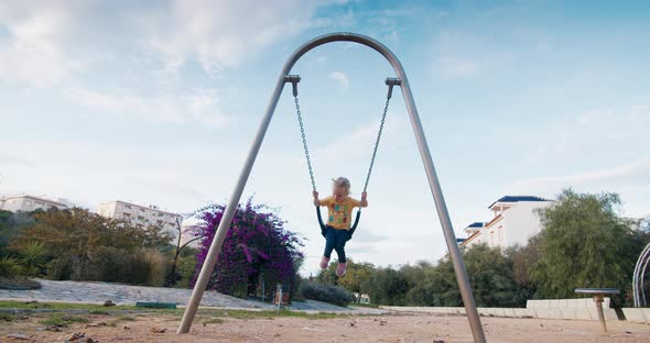 Slow motion cute european baby girl swinging on swing on chains in city park alt
