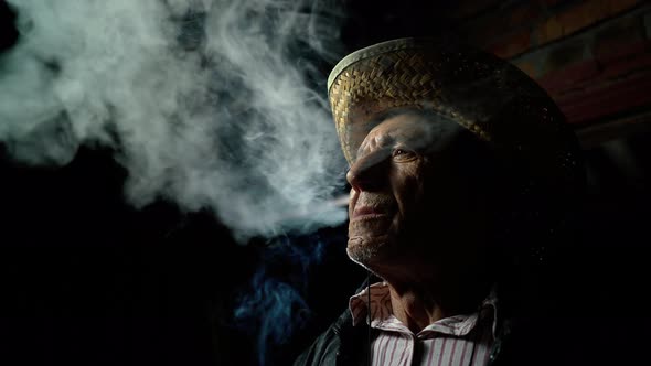 The man smokes a cigar. An elderly farmer in a straw hat smokes a cigar outside the ranch alt