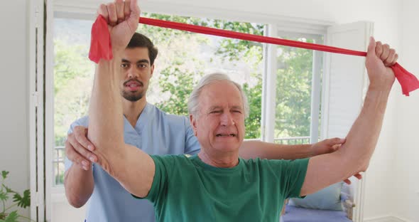 Biracial male physiotherapist with caucasian senior man holding resistance band while exercising alt