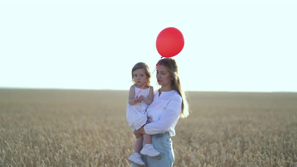 Mother with Daughter and Balloons Walking on Wheat Field