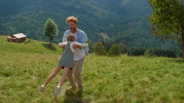 Happy Father Circling Daughter Sunny Day on Green Grass Mountain Meadow alt