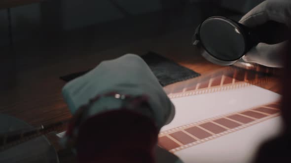 A man checks the quality of film tape with a magnifying glass. alt