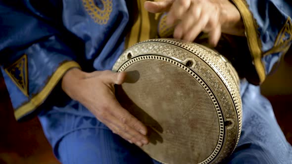 Tight shot of man in Moroccan dress playing arabic doumbek, darbuka, or derbeki alt