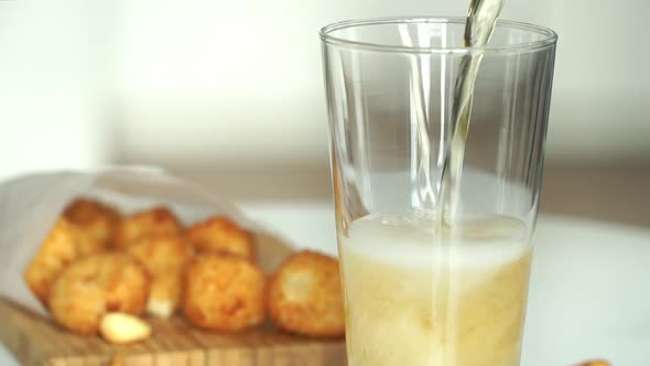 Beer is Poured Into Glass on Background of Appetizing Puffy Breaded Cheese Balls alt
