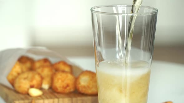 Beer is Poured Into Glass on Background of Appetizing Puffy Breaded Cheese Balls