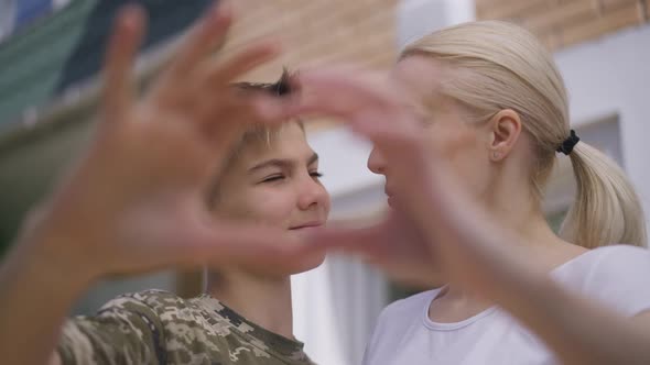 Closeup Heart Shape Hands with Woman and Boy Smiling Looking at Camera at Background alt