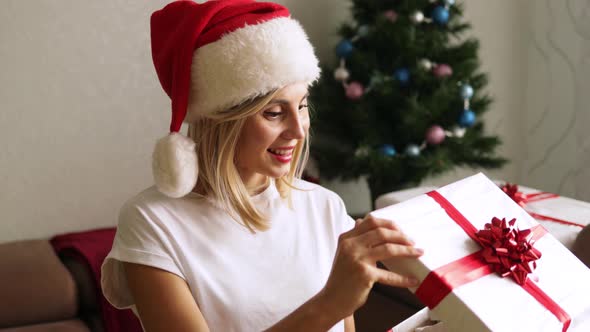 Smiling woman in Santa Claus hat holding white gift box