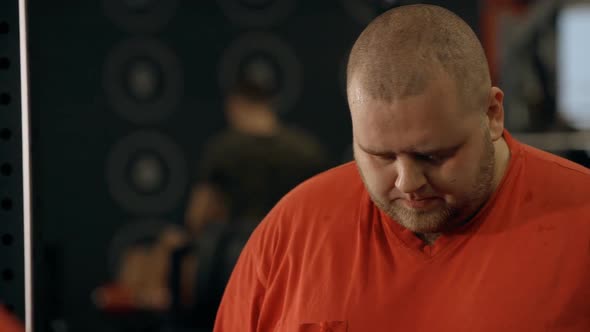 Overweight Man Looks at Himself in the Mirror of the Gym alt